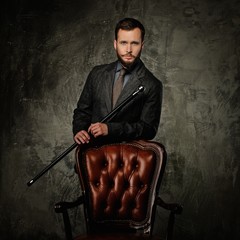 Handsome well-dressed man with stick near chair