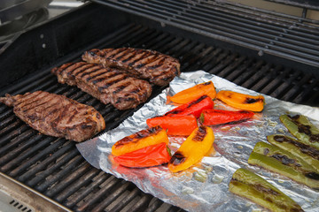 Grilling steaks and colorful peppers on foil