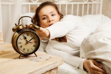 Woman in bed turning off alarm clock