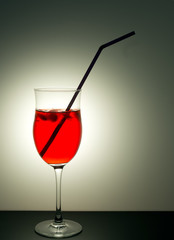 Red cocktail drink with straw backlit, grey background.