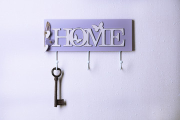 Old key hanging from hook, on light wall background