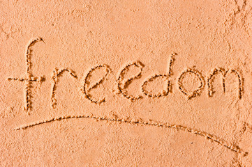 Freedom written on wet sand at the sea