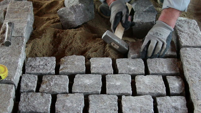 Mason worker making sidewalk pavement with granite blocks