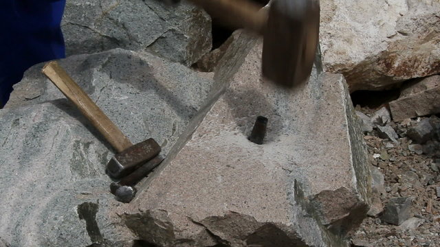 Stonemason cutting a block of granite with wedges and a hammer