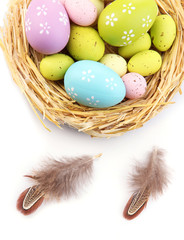 Easter eggs in nest and decorative feathers, isolated on white