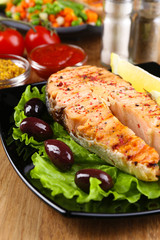Tasty grilled salmon with lemon and vegetables, on wooden table