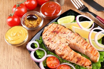 Tasty grilled salmon with lemon and vegetables, on wooden table