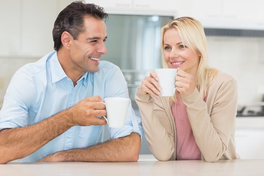 Happy couple with coffee cups in kitchen