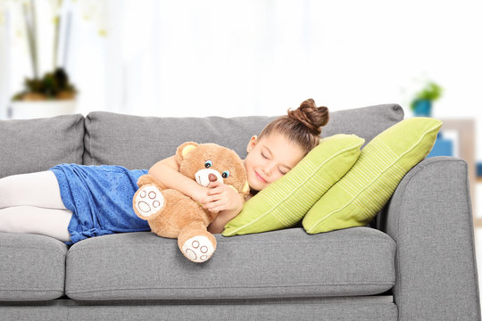Little girl sleeping on couch with teddy bear