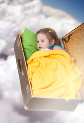 Dreaming girl flying in the cloudy sky in an old suitcase