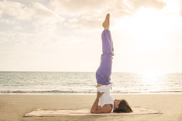Young woman practicing yoga candle pose on the beach near the oc