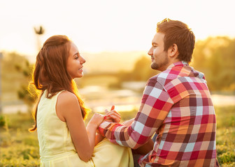 back view of young happy couple sitting on river at sunset