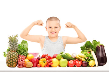 Boy showing muscles behind pile of vegetables