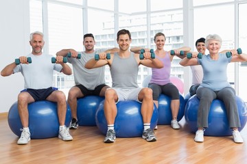 Fototapeta premium Fitness class with dumbbells sitting on exercise balls in gym