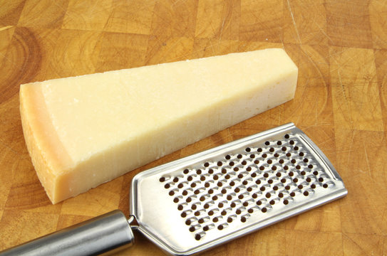 Parmesan cheese and grater on kitchen board.