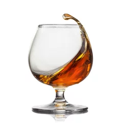 Gordijnen Splash of cognac in glass isolated on white background © artjazz