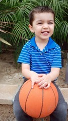 Cute mixed-race boy smiles as he waits to play basketball.