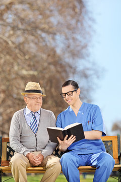 Male nurse reading to a pensioner in park