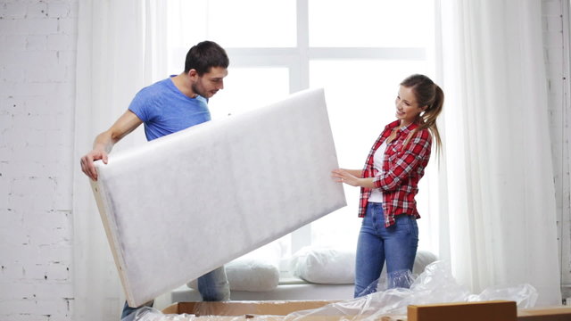 smiling couple opening big cardboard box with sofa