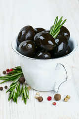 black olives in a metallic cup on wooden surface