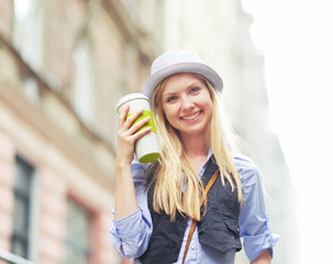 Happy young hipster with cup of hot beverage in the city