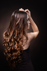 Fototapeta premium Beautiful young woman with long hair on dark brown background