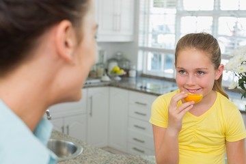 Obraz premium Girl having orange while looking at mother