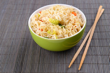Tasty instant noodles with vegetables in bowl on table close-up
