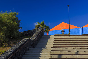 Fototapeta premium Treppe am Hafen von Alcola auf der Insel Teneriffa mit einem farbenfrohen Gebäude bei blauem Himmel