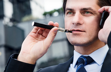 Businessman is smoking electronic cigarette outdoor - 63064128