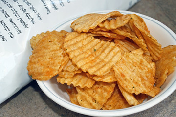 A bowl of spicy barbecued rippled potato chips beside bag