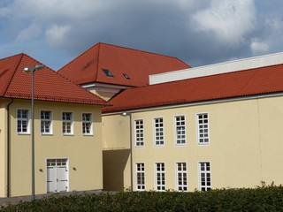 Altes saniertes Fabrikgebäude mit Fassade in Beige und Naturfarben mit Regenwolke im Sonnenschein...
