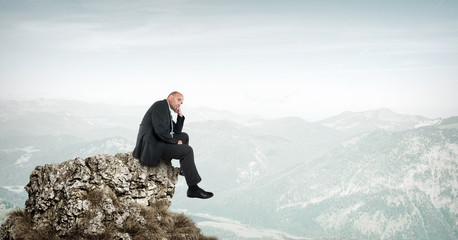 Businessman sitting on a rock in the mountains