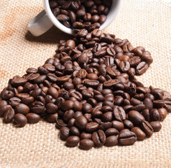 white cup with coffee beans on burlap background.