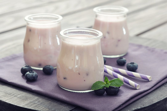 Yogurt with ripe fresh blueberry in jars on wooden background