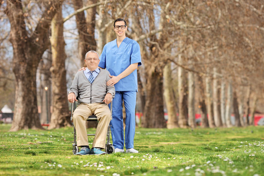Man in a wheelchair and male nurse posing in park