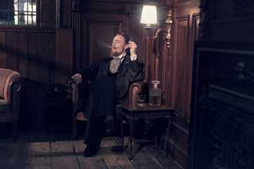 Vintage 1900 fashion man with beard. Sitting in old wooden readi