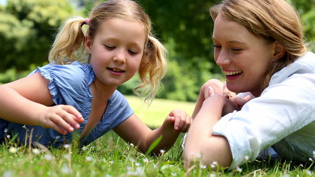 Happy mother lying on the grass with her little girl in the