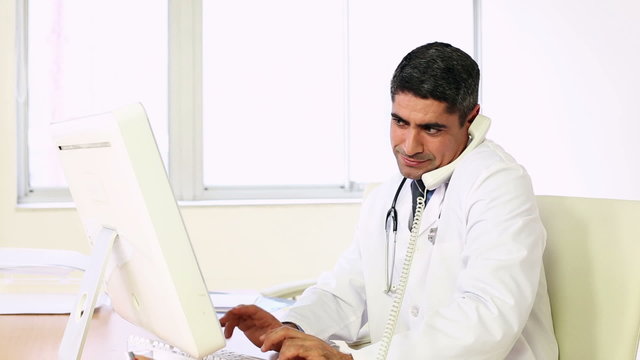 Doctor working at his computer and talking on phone