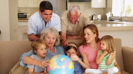 Extended family looking at globe together on couch - Powered by Adobe