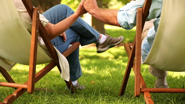 Retired couple sitting in deck chairs holding hands
