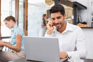 Obraz premium Man using laptop and mobile phone in coffee shop