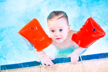 Cute toddler having fun in a swimming pool wearing red armbands