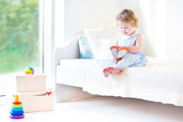 Obraz na płótnie Canvas Adorable toddler girl reading a book sitting on a white bed