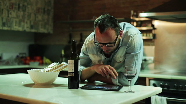 Young man with tablet computer drinking wine in the kitchen