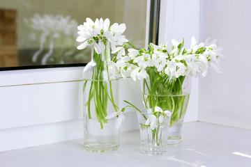 Beautiful bouquets of snowdrops in vases on windowsill