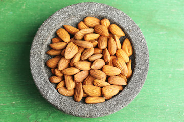 Almonds in bowl on color wooden background