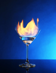 Glass with burning alcohol on blue background