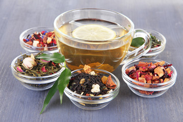 Cup of tea with aromatic dry tea in bowls on wooden background