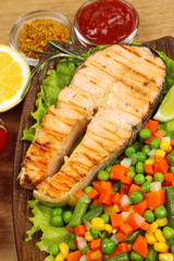 Tasty grilled salmon with vegetables, on wooden table